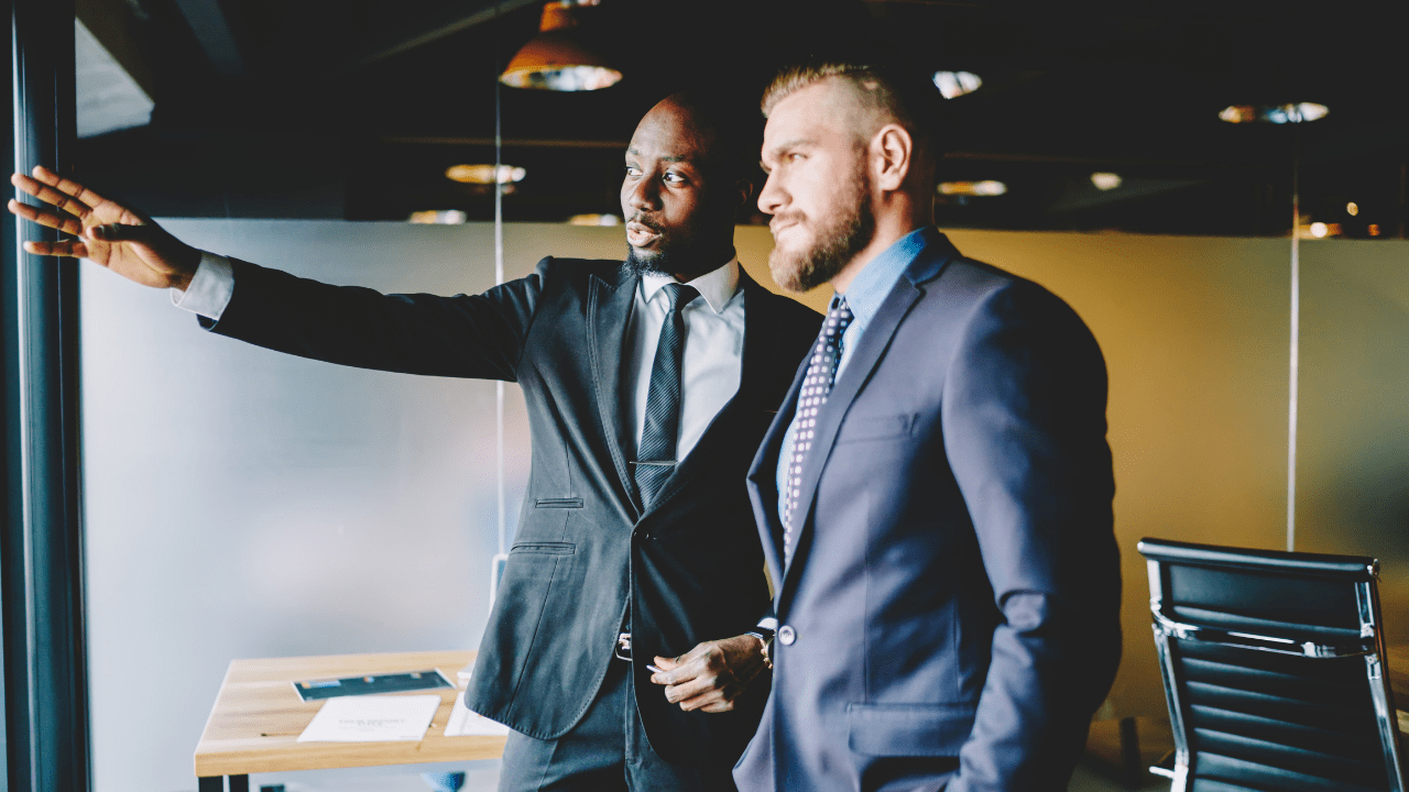 Two employees discussing strategy, wearing suits and standing in an office